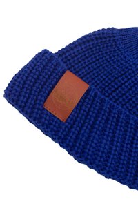 Niebieska dziana czapka z teksturowanym wzorem, z brązową skórzaną łatą z logo. Rękaw jest prążkowany, a materiał wydaje się miękki.