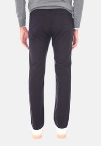 Pantaloni in cotone viola scuro con design a gamba dritta, dotati di due tasche posteriori e dettagli di cucitura sottili, abbinati a sneakers bianche.