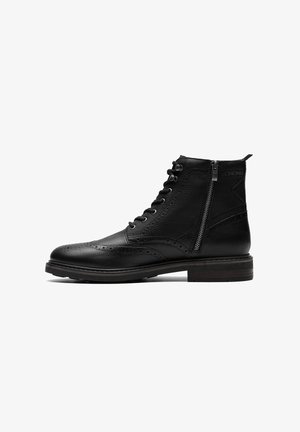 Zwarte leren enkelboot met brogue-details, vetersluiting aan de voorkant, zijrits en een gestructureerde afwerking. Voorzien van een gestapelde houten hak.