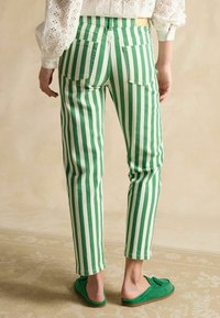 Zeleno-biele pruhované nohavice z textúrovaného materiálu, s dvoma zadnými vreckami a úzkym strihom. Nosia sa so zelenými slip-on topánkami.