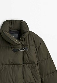 Olijfgroene gewatteerde jas met een hoge kraag, voorzien van een zijrits en een metalen sluiting. Zachte, gewatteerde textuur met zakken.