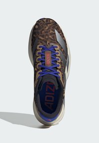 Chaussures de sport avec imprimé léopard marron et accents gris, lacets violets et étiquette "ADIZERO" rouge. Intérieur noir rembourré et semelle légère.