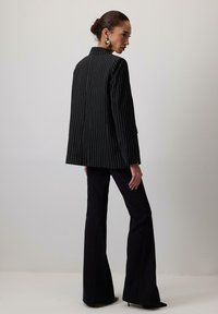 Sacou negru cu dungi subțiri, cu un croi lejer, purtat peste pantaloni negri evazați, are un guler înalt și accente pe umeri. Textură de țesătură netedă.