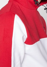 Czerwono-biały sweatshirt z kolorowym blokiem, z wysokim kołnierzem, teksturowanym materiałem i szczegółami kaptura ze sznurkiem.