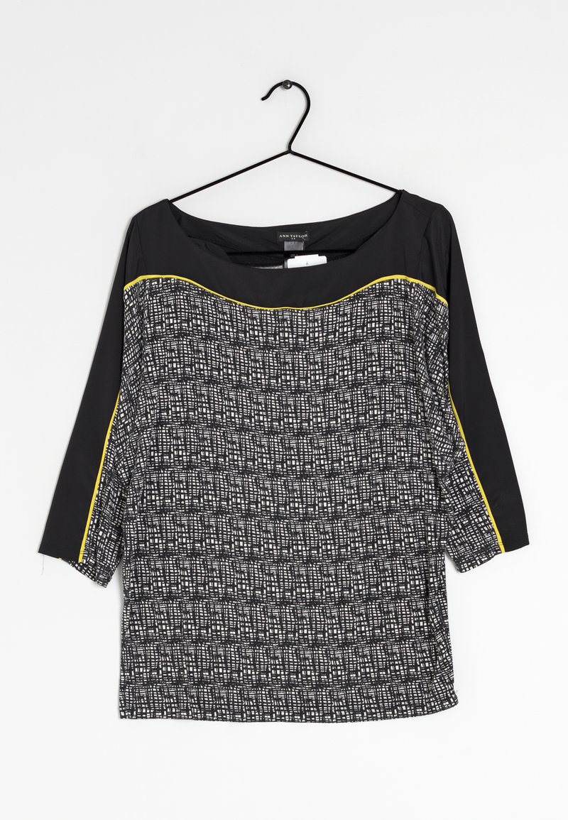 Sort og mønstret top med trekvartærmer, fremstillet i et tekstureret stof med hvide og grå firkanter, samt en gul accent nær halsudskæringen.