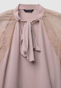 Blush-pink Bluse mit Spitzen-Schultern und einer gebundenen Schleife am Ausschnitt, die zarte florale Spitzenmuster präsentiert.