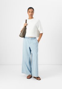 White cropped, short-sleeve shirt with relaxed fit; light blue wide-leg jeans with elastic waistband; brown flat sandals; brown shoulder bag.