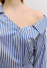 Blau-weiß gestreiftes Hemd mit einem Schulterdesign, Knopfverschlüssen und weichem Stoff. Mit Kragen und asymmetrischem Schnitt.