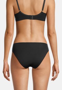 Slip in bikini neri con una texture liscia e forma a vita bassa, caratterizzato da linee pulite e dettagli minimal, abbinato a un reggiseno nero.