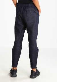 Granatowe spodnie dresowe o teksturowanym wykończeniu, z elastycznym pasem, tylnymi kieszeniami i zamkami na kostkach, zestawione z czarnymi sneakersami.