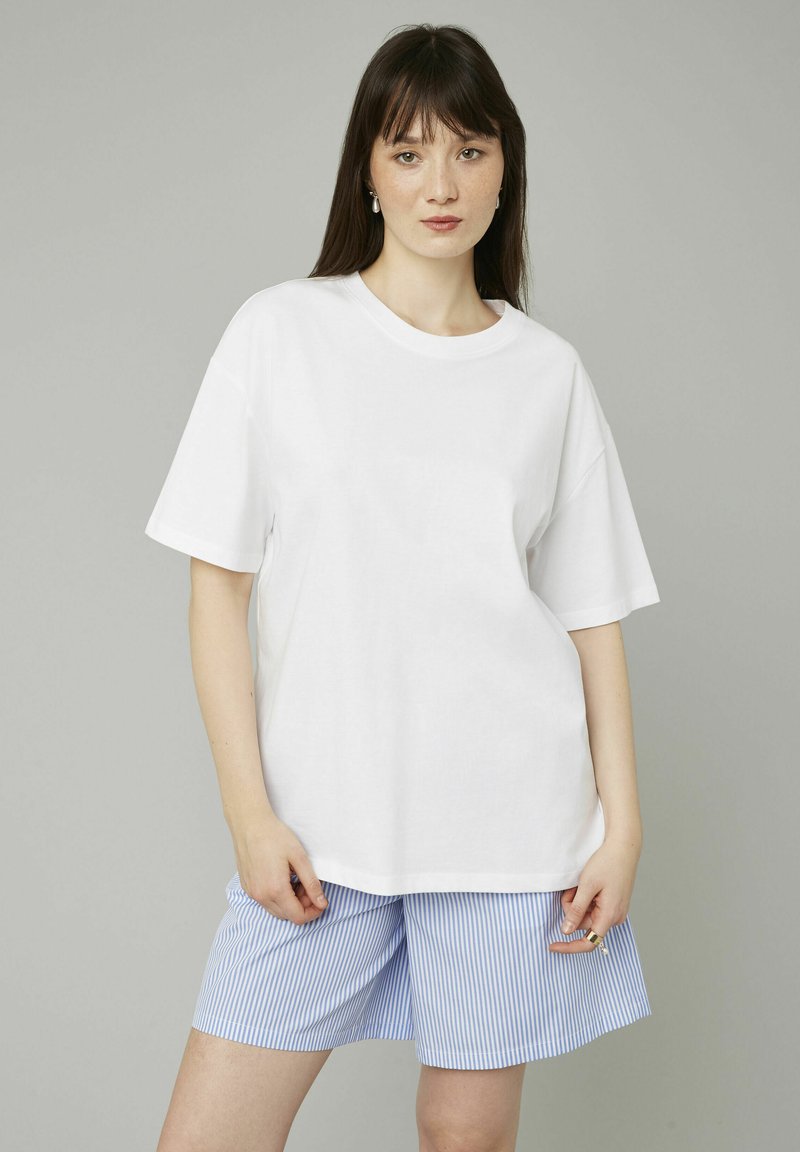 T-shirt blanche oversize à manches courtes, associée à un short rayé bleu et blanc. Design simple, en coton, coupe décontractée.