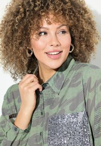 Groen patroon shirt met een glanzende zilveren paillettenzak en tekstafdruk, met een knoopsluiting en lange mouwen.