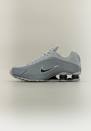 Chaussure de sport Nike grise avec logo swoosh noir et blanc, design à lacets et coussinage unique en forme de ressort au niveau du talon de la semelle.