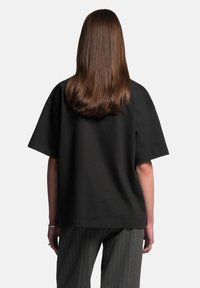 Černé oversize tričko s krátkými rukávy, kulatým výstřihem a jednoduchým designem, doplněné pruhovanými šedými kalhotami.