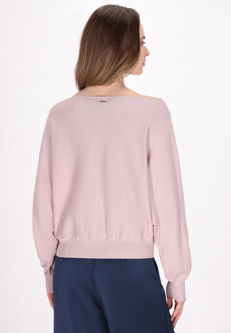 Overmaatse roze gebreide trui met geribde zoom en mouwen. Heeft een brede halslijn en textuurstof. Gemaakt met donkerblauwe broeken.