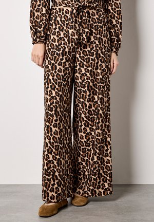 Szerokie spodnie z nadrukiem w panterkę wykonane z miękkiego materiału, z ściągaczem w pasie. Charakteryzują się beżowym tłem, czarnymi i brązowymi plamami oraz luźnym fasonem.