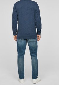 Suéter azul oscuro con acabado texturizado, mangas largas y dobladillo redondeado, combinado con jeans de mezclilla azul claro. Zapatillas blancas visibles.