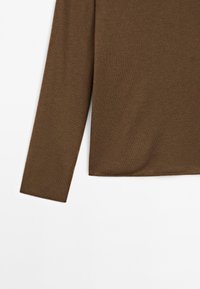 Manche et bas du torse d'un pull en maille marron à manches longues sur fond blanc, mettant en valeur la texture du tissu et l'ourlet droit.