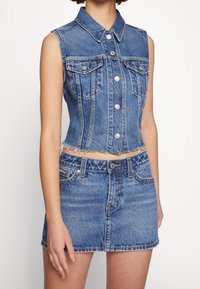 Jeansklänning utan ärmar och matchande kjolset. Ljusblå tvätt, figurnära design med fransad fåll, framfickor och silverfärgade knappdetaljer.
