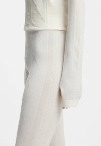 Dopasowany top z długim rękawem wykonany z kremowej tkaniny o fakturze z ozdobnymi wzorami. Legginsy mają pionowe paski i zygzakowate motywy w dopasowanym kolorze.