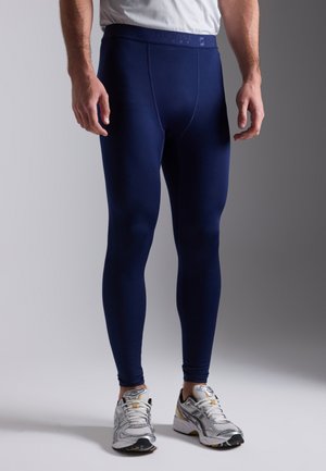 Leggings sportivi blu navy con una texture liscia e un design aderente. Vita alta, cuciture minime, abbinati a scarpe da ginnastica bianche e argentate.