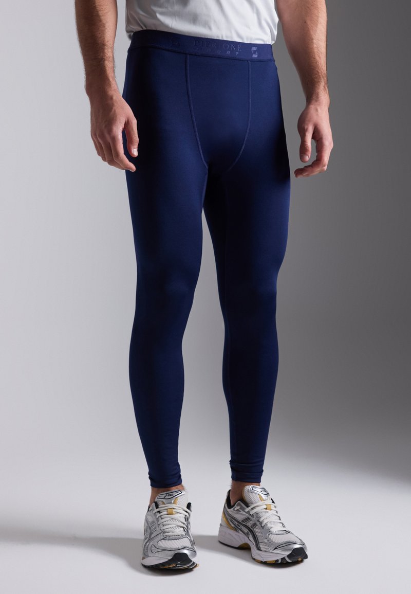 Marineblauwe sportleggings met een gladde textuur en een aansluitend ontwerp. Hoge tailleband, minimale stiksels, gecombineerd met witte en zilveren sportschoenen.