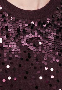 Burgundyröd tröja prydd med olika nyanser av cirkulära paljetter, med en mjuk stickad textur och design med rundad hals.