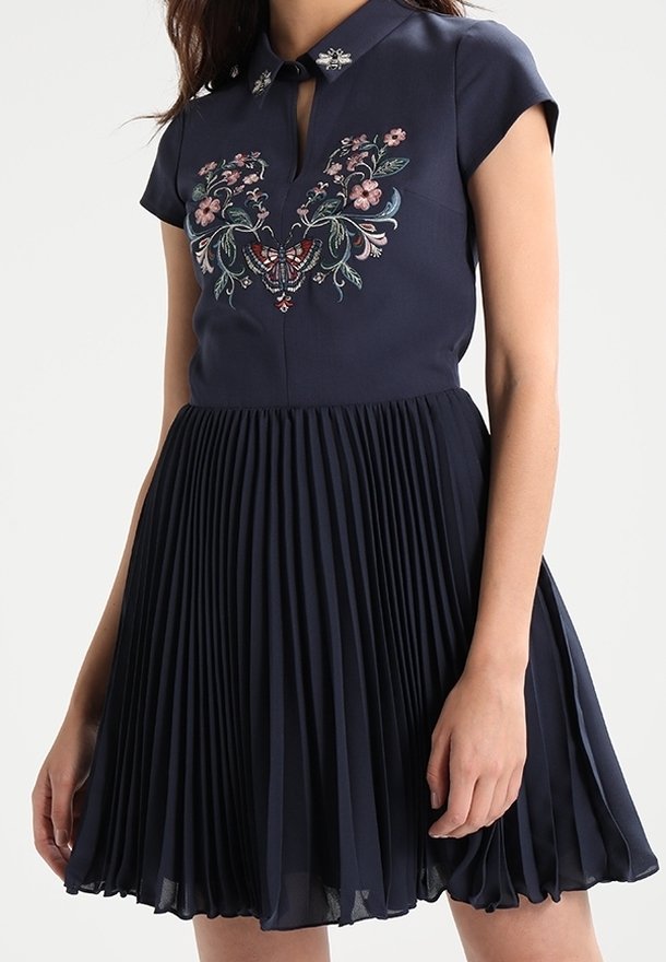 Robe bleu marine avec jupe plissée, broderies florales et papillons sur la poitrine, et embellissements en forme d'abeilles sur le col.