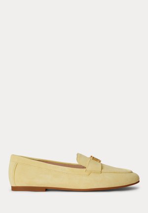Gelber Wildleder-Flachloafer mit kleinem goldfarbenem Schnallendetail und brauner Sohle, von der Seite auf weißem Hintergrund gezeigt.