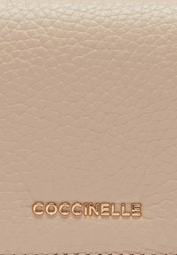 Portafoglio in pelle rosa chiaro con trama, con il nome del marchio "COCCINELLE" impresso in oro in modo visibile. Presenta una finitura liscia e una grana sottile.