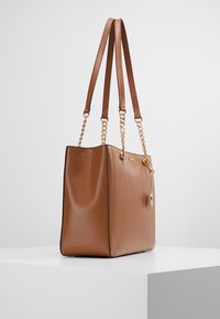 Bruine, gestructureerde leren tote bag met dubbele platte handvatten en gouden kettingaccenten. Vierkante vorm, ritssluiting en pendantdetail aan de zijkant.