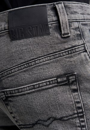 Melnas denima bikses ar teksturētu apdari, lielu ādas birku un mazāku zīmola birku pie aizmugurējā kabatas.