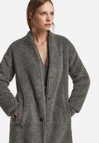 Grå, struktureret, lang frakke med klapkrave, frontknapper og sidelommer; lavet af et blødt, fuzzy materiale.