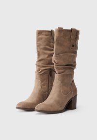 Botas de ante marrón hasta la rodilla con un diseño arrugado, cremallera lateral y tacón apilado. Presenta una lengüeta para facilitar el calzado.