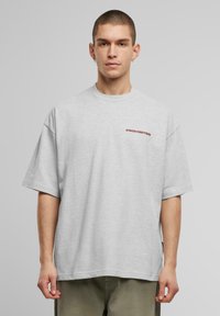 Tricou oversized gri din bumbac, cu mâneci scurte și guler rotund. Pe piept este imprimat cu litere în roșu închis cuvântul "PROHIBIT".