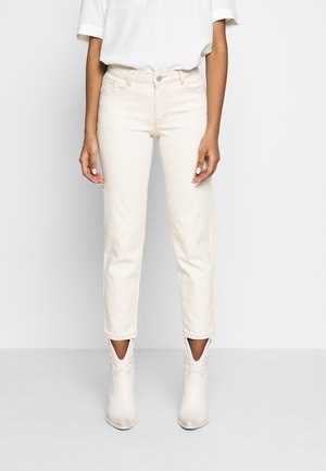 Jeans de talle alto color beige con corte recto, que cuentan con bolsillos traseros y dobladillos enrollados. Combinados con botas de tobillo color blanco apagado.