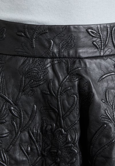 Jupe en cuir noir avec une broderie florale texturée, dotée d'une taille lisse et de détails complexes sur la surface du tissu.