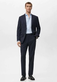 Completo blu navy dal taglio slim, con rever a intaglio, singolo bottone e due tasche, abbinato a una camicia azzurra e scarpe nere.