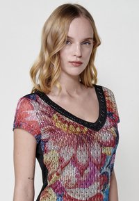 Top de punto multicolor con escote en V, mangas cortas y un cuello negro decorado. La tela tiene una apariencia texturizada y con patrón.