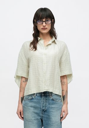 Cămașă verde deschis cu mâneci scurte, cu nasturi, dintr-un material texturat. Are guler și croială lejeră. Asortată cu blugi din denim albastru deschis.