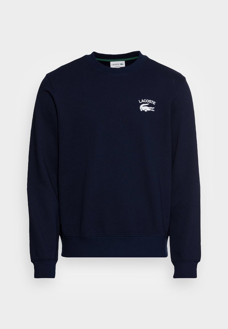 Sweat-shirt Lacoste bleu marine avec col rond, manches longues, poignets et ourlet côtelés, et logo Lacoste blanc sur la partie supérieure gauche de la poitrine.