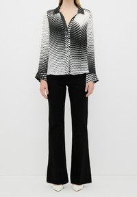 Black and white button-up shirt with a polka dot gradient pattern, long sleeves, and flared cuffs, paired with black flared pants.