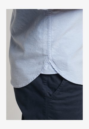 Lichtblauwe katoenen shirt met een afgeronde zoom, gestikte details, gecombineerd met donkerblauwe broek met zijzakken. Zachte textuur.