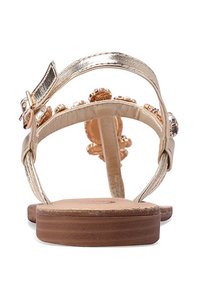 Sandali metallici dorati con una sottile cinghia, dettagli di perline e una suola piatta in legno. La vista posteriore mette in evidenza gli elementi decorativi e la fibbia regolabile.