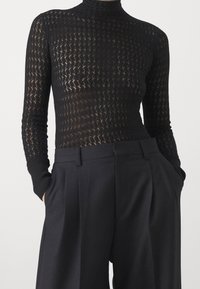 Pull noir ajusté à manches longues avec un motif en maille ouverte texturée. Associé à un pantalon noir taille haute plissé.