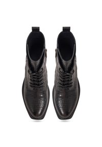 Bottes noires à cheville avec texture crocodile, lacets à l'avant, fermeture éclair latérale et languettes de traction, vues de dessus sur fond blanc.