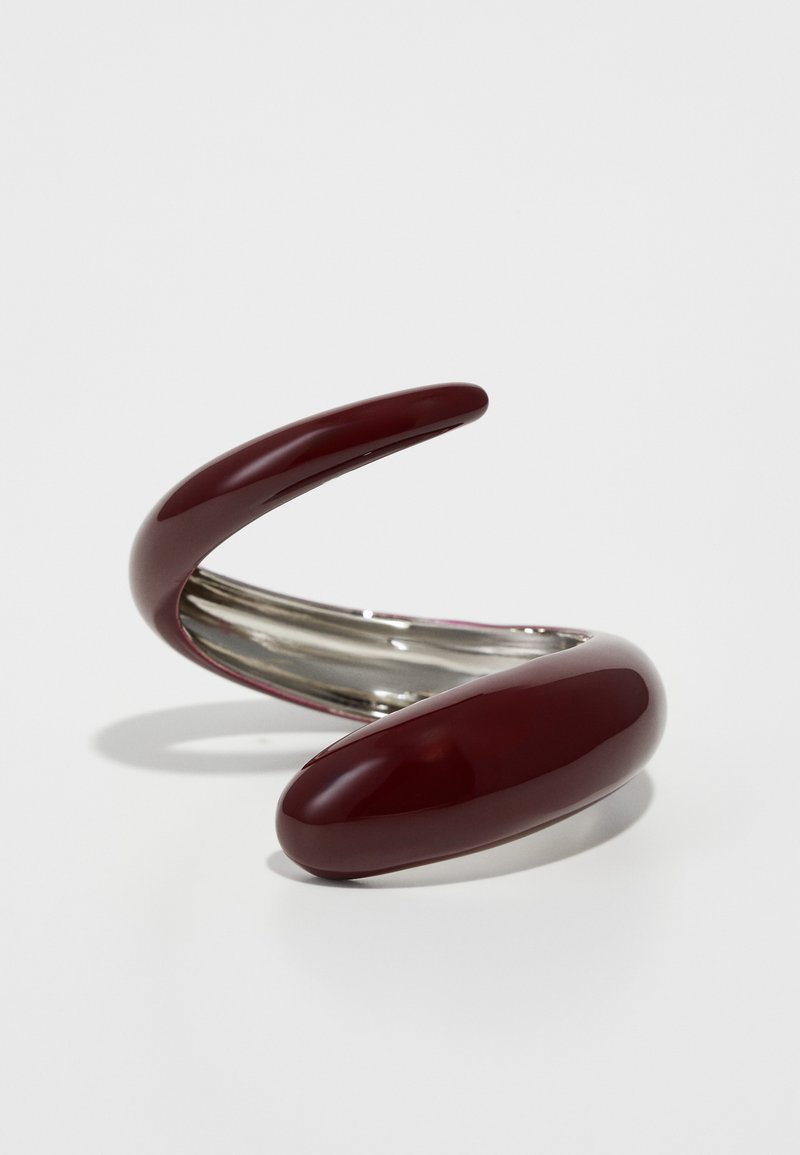 Burgunder, glinsende metallarmbånd med en buet, vridd design. Glatt tekstur med reflekterende rustfritt stål detaljer på innsiden.