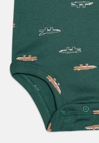 Bodysuit en coton vert avec des motifs de crocodile et de sous-marin en blanc et marron. Dispose de fermetures à pressions et de bords côtelés. Texture douce.
