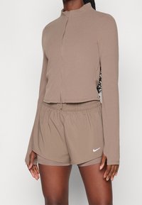 Brown athletic zip-up jacket with long sleeves paired with matching elastic waistband shorts. Features Nike logo in white. Smooth texture.