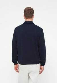 Sötétkék pulóverdzseki gallérral, rugalmas mandzsettákkal és szegéllyel; puha anyagból készült, sima textúrával és látható minták nélkül.